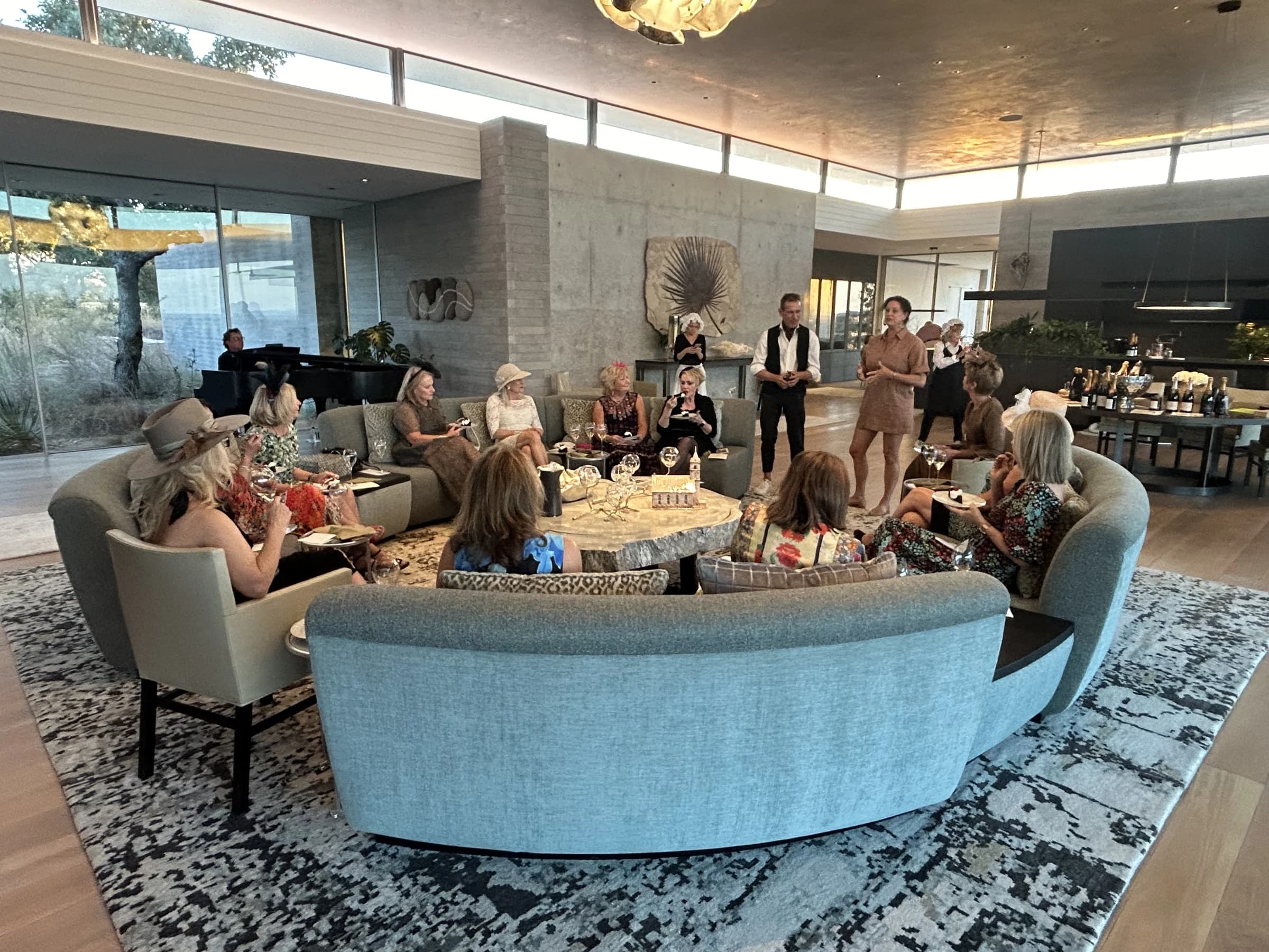 An intimate private wine tasting in a stunning modern home — guests gathered around a curved sofa as the sommelier presents.
